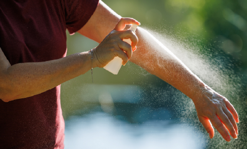 photo of a person spraying insect repellent on themselves 