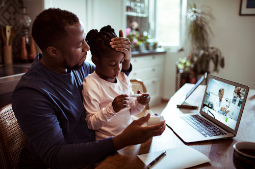 A father checking his daughters temperature while having a video call with a doctor